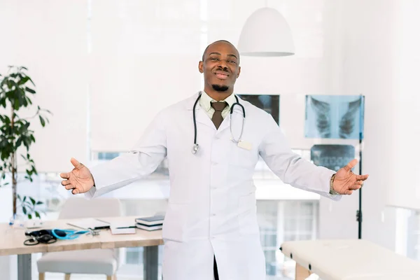 Jeune homme médecin afro-américain regardant la caméra souriant à bras ouverts pour un câlin. Expression joyeuse embrassant le bonheur. Bienvenue à l'hôpital — Photo