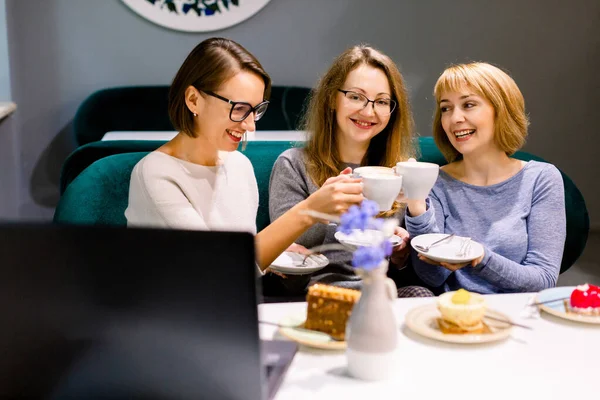 Ženy přátelé při pohledu na dorty, tři dívky přátelé pití kávy v kavárně a jíst dezerty, ženy během oběda práce na notebooku v kavárně — Stock fotografie