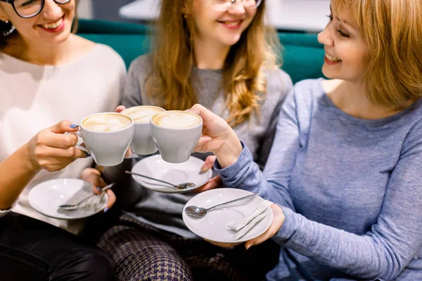 Drinking coffee together. Top view of tree beautiful women keeping cups of coffee in hands and smiling. Women in cafe indoors. Meeting of best friends. Coffee with cakes