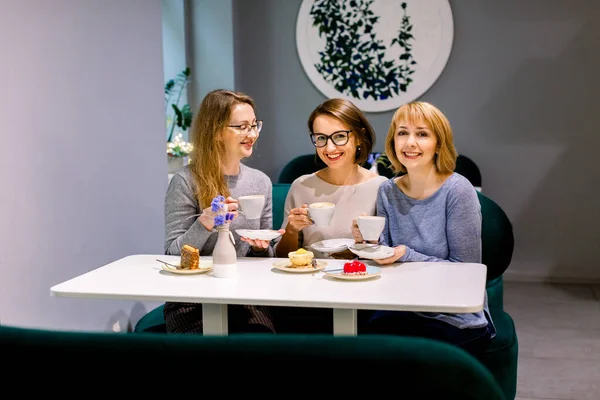 Tree young pretty women best friends. Horizontal shot of beautiful women talking and having fun while drinking coffee and eating desserts in cafe. Women friends gossiping during coffee time.