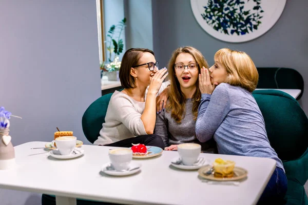 En iyi arkadaşlarla dedikodular. Kafede keklerle kahve içerken üçüncü arkadaşlarının kulaklarına fısıldayan iki güzel kadının yatay çekimi. Kadın arkadaşlar kahve saatinde dedikodu yapıyorlar.. — Stok fotoğraf