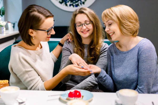 Hezká mladá žena ukazuje zásnubní prsten svým dvěma nejlepším přátelům v kavárně slaví — Stock fotografie