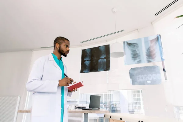 Jeune médecin afro-américain professionnel examinant les rayons X de patients dans une clinique hospitalière moderne — Photo