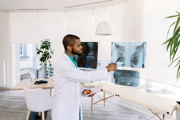 Médecin afro-américain en uniforme médical avec radiographie. Jeune médecin afro-américain professionnel examinant la radiographie de la poitrine des patients — Photo