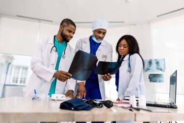 Radyoloji, insanlar ve tıp konsepti. Üç Afrikalı doktor, cerrah ve radyologdan oluşan bir grup. Hastanedeki röntgen görüntülerine bakıp tartışıyorlar.