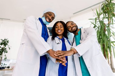 Üç Afrikalı genç doktor hastanede el ele tutuşuyorlar, konsept ekip çalışması, mutlu doktorlar motivasyon ve sağlık hizmetleri için birlikte çalışıyorlar.
