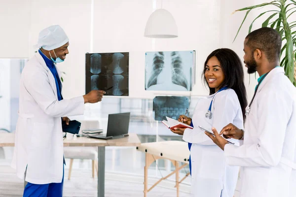 의료, 의료: 아프리카 의사들의 모임 이 클리닉이나 병원에서 X-ray 를 토론하고 찾고 있습니다. 수석 의사인 아프리카 남자가 두 명의 젊은 의사 와대 화를 나누고 있다 — 스톡 사진