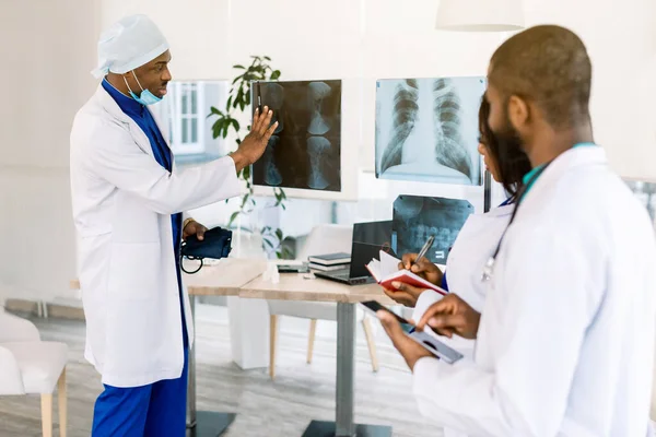 Soins de santé, médical : Groupe de médecins africains discutent et regardent les rayons X dans une clinique ou un hôpital. Africain homme médecin en chef discuter avec ses deux jeunes médecins résidents — Photo