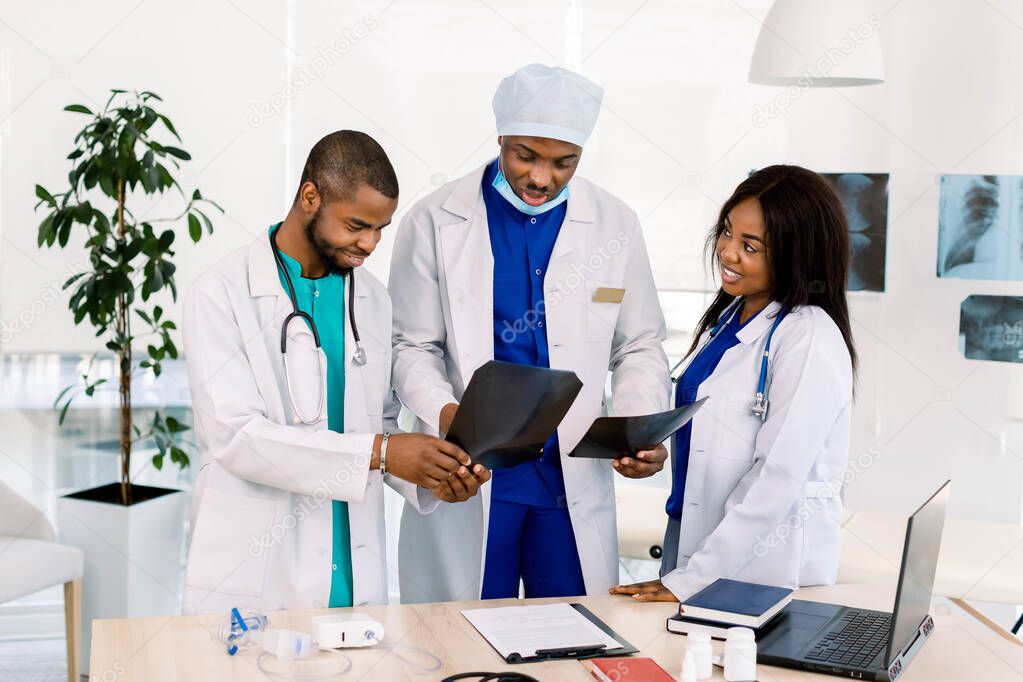 Medical doctors looking at x-rays in a hospital. African man surgeon checking x ray film at office with male and female doctors radiologists residents.