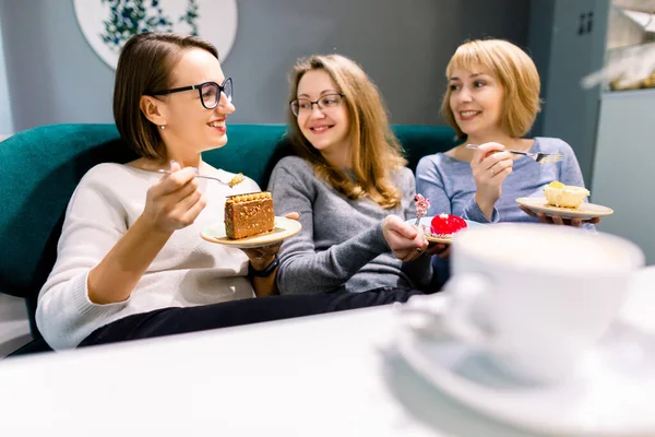 Setkání s nejlepším přítelem. Horizontální záběr krásné tři ženy mluví při pití kávy s dezerty v vintage kavárně. Ženy přátelé drbání během kávy. — Stock fotografie