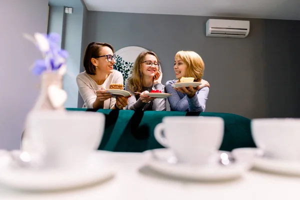 Setkání s nejlepším přítelem. Horizontální záběr krásné tři ženy mluví při pití kávy s dezerty v vintage kavárně. Ženy přátelé drbání během kávy. — Stock fotografie