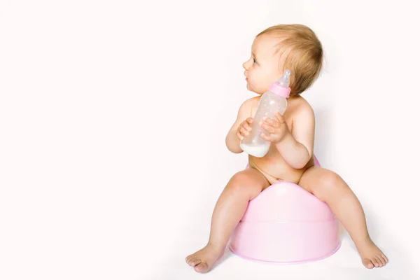 Foto encantadora de bebê bonito menina segurando uma boottle com leite de bebê e sentado em um penico rosa. Isolado sobre fundo branco — Fotografia de Stock