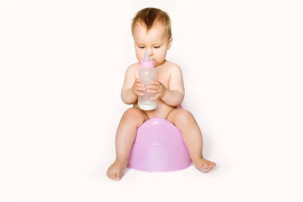 Foto encantadora de bebê bonito menina segurando uma boottle com leite de bebê e sentado em um penico rosa. Isolado sobre fundo branco — Fotografia de Stock