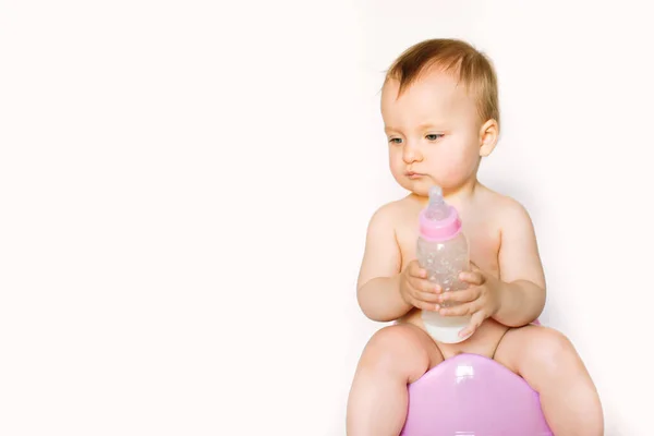 Foto encantadora de bebê bonito menina segurando uma boottle com leite de bebê e sentado em um penico rosa. Isolado sobre fundo branco — Fotografia de Stock