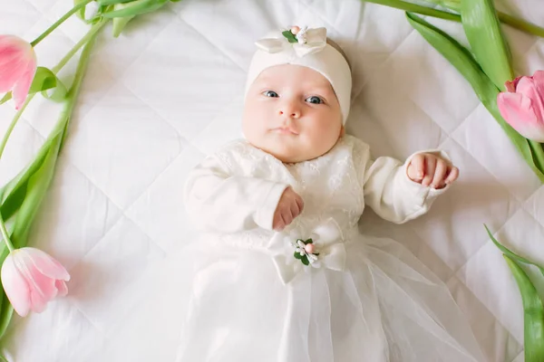 A kis gyönyörű újszülött lány fekszik az ágyon a virágok között. — Stock Fotó