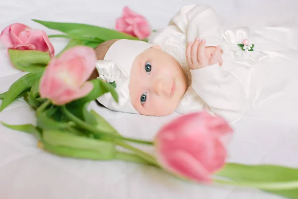 Pequena menina recém-nascida bonita deitada na cama entre as flores — Fotografia de Stock