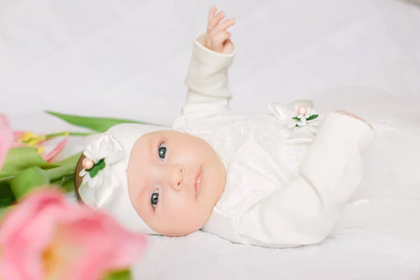 Klein mooi pasgeboren meisje liggend op het bed tussen de bloemen — Stockfoto