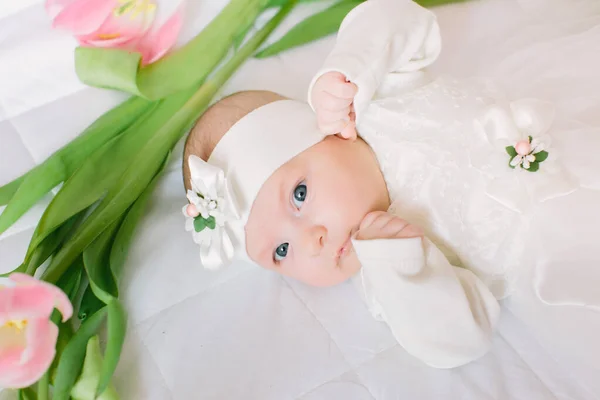 Pequena menina recém-nascida bonita deitada na cama entre as flores — Fotografia de Stock