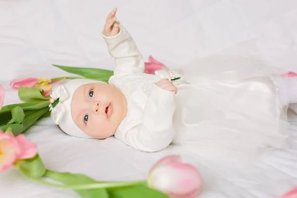 Pequena menina recém-nascida bonita deitada na cama entre as flores — Fotografia de Stock