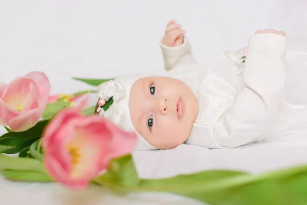 Pequena menina recém-nascida bonita deitada na cama entre as flores — Fotografia de Stock