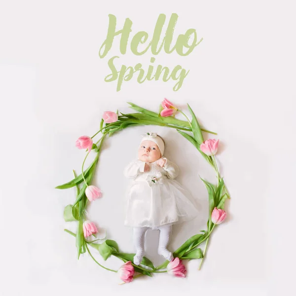 Mała piękna nowonarodzona dziewczynka leżąca na łóżku pośród kwiatów i napisu Hello Spring — Zdjęcie stockowe