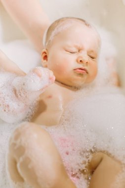 Mutlu gülen bebek köpüklerle banyo yapıyor. Küvette küçük bir çocuk. Bebek yıkama ve banyo..