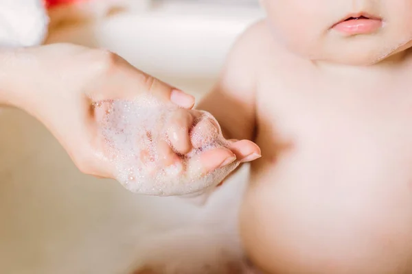 Feliz bebê rindo tomando um banho brincando com bolhas de espuma. Criança em uma banheira. Lavagem infantil e banho. Mãe irreconhecível banhando seu bebê em branco pequeno morcego de plástico . — Fotografia de Stock