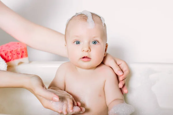 Happy laughing baby taking a bath playing with foam bubbles. Little child in a bathtub. Infant washing and bathing. Hygiene and care for young children. Newborn baby bathing — Stock Photo, Image