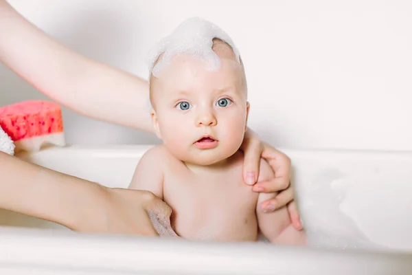 Happy laughing baby taking a bath playing with foam bubbles. Little child in a bathtub. Infant washing and bathing. Hygiene and care for young children. Newborn baby bathing — Stock Photo, Image