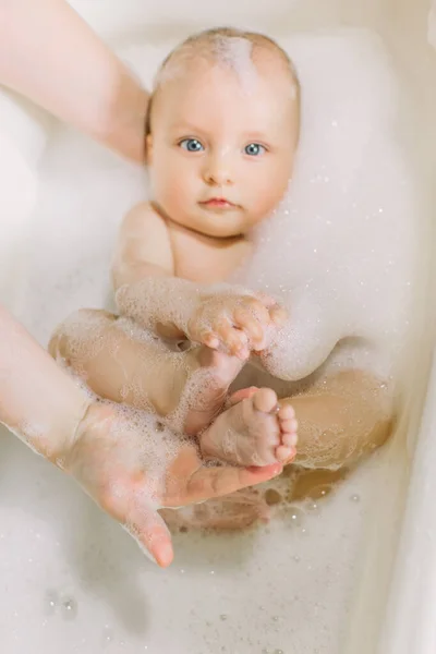 Glücklich lachendes Baby, das ein Bad nimmt und mit Schaumblasen spielt. Kind in der Badewanne. Säuglingswäsche und Baden. Baby blickt in einer Plastikwanne voller Schaum nach oben. — Stockfoto