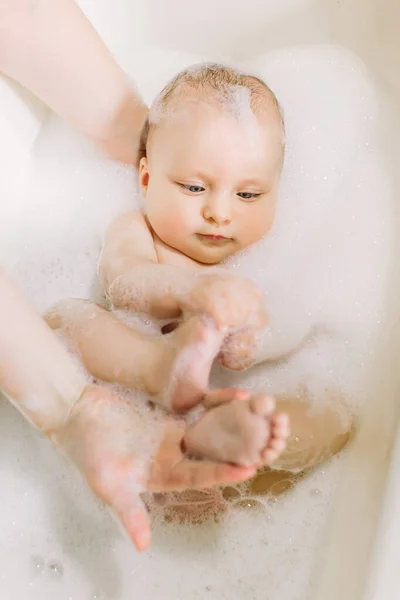 Happy laughing baby taking a bath playing with foam bubbles. Little child in a bathtub. Infant washing and bathing. Baby looking upwards in a plastic tub full of foam. — Stock Photo, Image