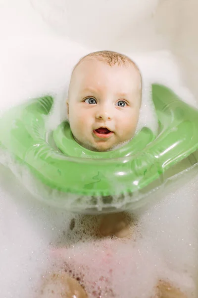 El bebé es recién nacido, la chica se está bañando en el baño con un círculo inflable alrededor de su cuello. —  Fotos de Stock
