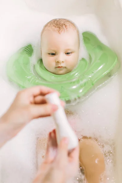 Baby swimming with green neck swim ring. mom squeezes shampoo out of the tube — Stock Photo, Image