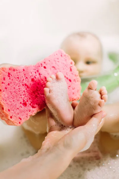 Baby swimming with green neck swim ring. mom rubs baby feet with a red sponge — Stock Photo, Image