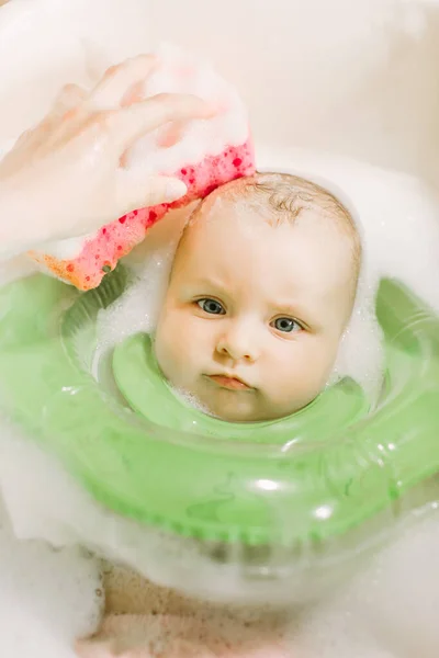 Μωρό κολύμβηση με δαχτυλίδι πράσινο λαιμό κολύμπι. Μαμά πλύσιμο κεφάλι μωρού με ένα κόκκινο σφουγγάρι — Φωτογραφία Αρχείου