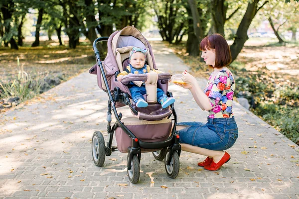 Η μαμά ταΐζει το παιδί περπατώντας με καροτσάκι στο πάρκο. . — Φωτογραφία Αρχείου
