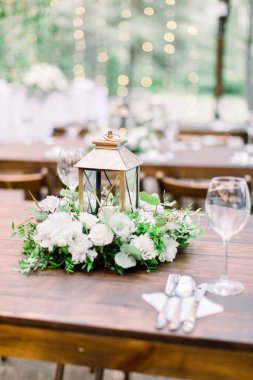 Düğün dekorasyonları ahşap masa, çiçek aranjmanı ve altın fener üzerinde. Sofra çatal bıçak takımı, çanak çömlek ve şarap kadehleriyle servis edilir..