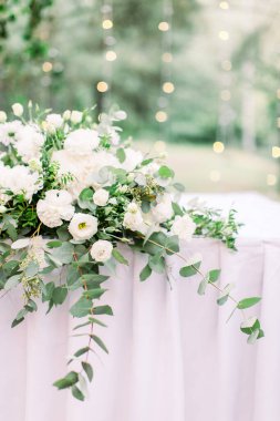 Masa örtüsüyle kaplanmış çiçek ve yeşillik süslemeli masa ayarları bahçede ya da ormanda, bulanık arka planda küçük ampuller.