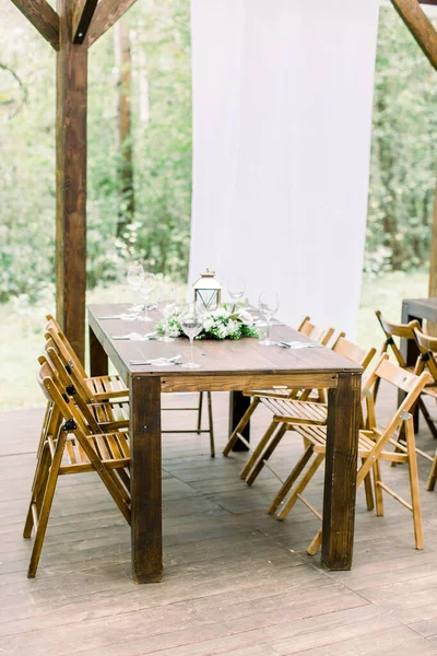 Mesa de madeira com decorações rústicas florais e lanterna dourada, em restaurante ao ar livre na floresta. Celebração de casamento ao ar livre em um restaurante. Cenário de mesa festiva, catering . — Fotografia de Stock
