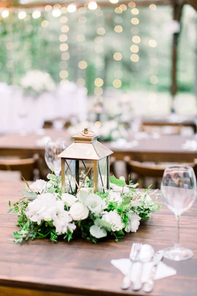 Hochzeitsdekorationen im rustikalen Stil auf Holztisch, Blumengesteck und goldener Laterne. Tisch mit Besteck und Geschirr, Weingläser. — Stockfoto