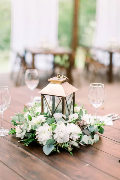 The composition of flowers and greenery, golden lantern in rustic style, standing on served table in the area of wedding party outdoors — Stock Photo, Image