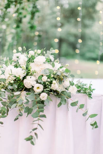 Ambiente de mesa com decoração de flores e vegetação, coberto com toalha de mesa, ao ar livre no jardim ou na floresta, pequenos bulbos de lípidos no fundo borrado — Fotografia de Stock