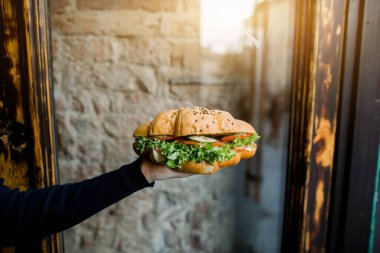 Şehir kafesindeki gri duvarın arka planında taze marul ve sebzeli kruvasan var.