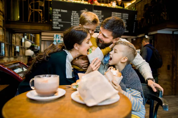 Mutlu komik aile, baba, anne ve iki tatlı çocuk, kafeteryada oturup, öğle veya kahvaltı ederken, taze kruvasan yerken ve gülerken, — Stok fotoğraf