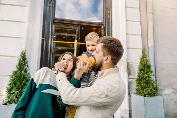 Щаслива сім'я, батько, мати і милий хлопчик, що стоїть разом і розважається на відкритому повітрі, насолоджується обідом і їсть свіжі круасани — стокове фото