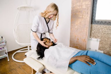 Çekici Afrikalı kız hastası için maske takan güzel kadın kozmetik uzmanının yan açılı portresi..