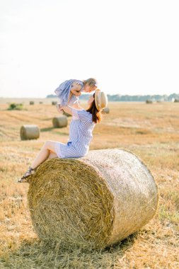 Benzer çizgili mavi elbiseler giyen, güzel bir tarlada saman demetinde oturan ve birlikte oynayan sevimli kızıyla birlikte genç ve çekici bir anne. Anne bebeğini elinde tutuyor.