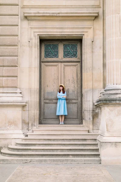 Menina bonita em vestido azul e chapéu em pé na frente da porta do vintage do edifício antigo — Fotografia de Stock