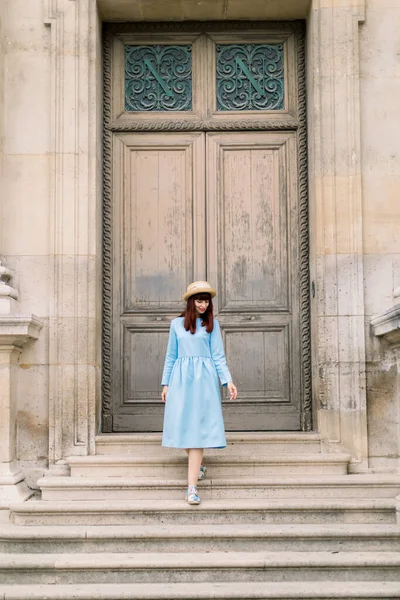 Foto di una bella giovane donna in abito blu scende le scale d'epoca sullo sfondo di un vecchio edificio con porte — Foto Stock