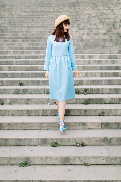 Jovem bela caucasiana ruiva mulher vestindo vestido azul elegante e chapéu de palha, descendo as escadas de pedra velha e desfrutar de caminhada na cidade europeia — Fotografia de Stock